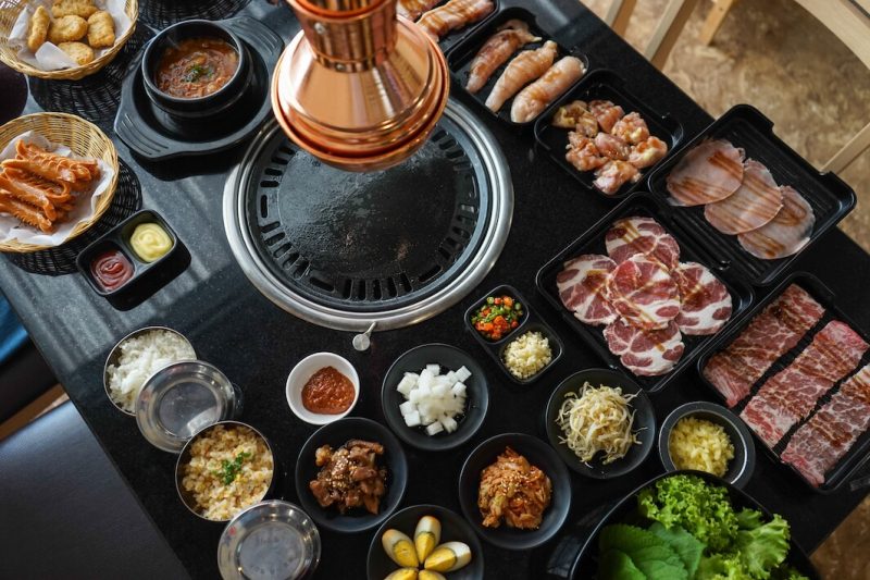Korean BBQ Grill, surrounded by bowls filled with a delicious selection of meats and vegetables ready to cook.